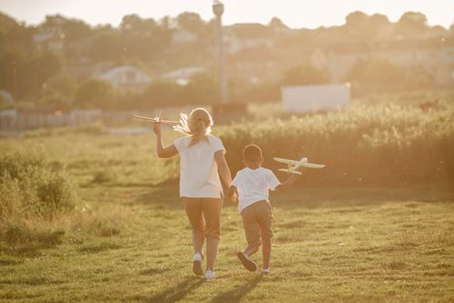 Free Two children playfully running with toy planes in a sunlit meadow. Stock Photo