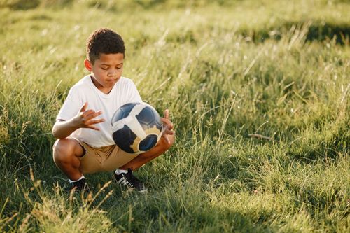 Free A young boy in a white shirt plays with a soccer ball in a sunny field, enjoying the outdoors. Stock Photo