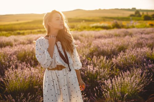 Free A serene portrait of a woman in a lavender field during sunset, wearing a white dress and looking tranquil. Stock Photo