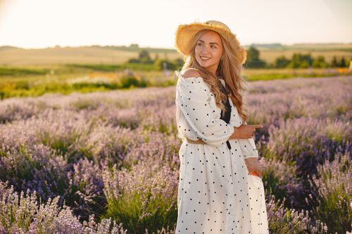 Free Smiling woman in a polka dot dress stands in a lavender field at sunset. Stock Photo
