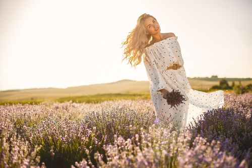 Free A joyful woman in a polka dot dress stands in a lavender field during sunset. Stock Photo