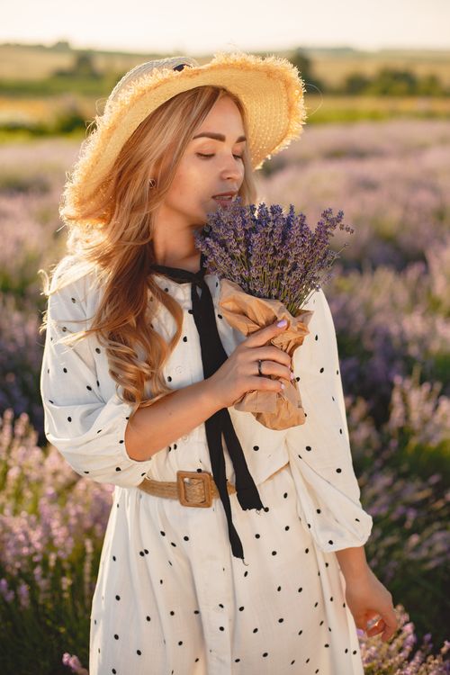 Free A serene portrait of a woman in a white dress and straw hat standing in a lavender field during summer. Stock Photo