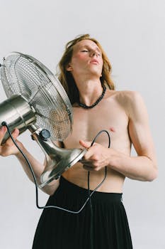 Stylish shirtless model holds a large electric fan indoors, capturing modern and fashion-forward concepts.