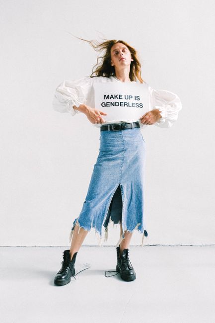 Person wearing a statement shirt and denim skirt, embracing genderless fashion on a white background.