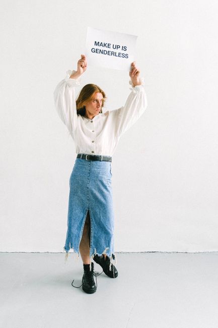 Person holding a sign promoting genderless makeup. Fashion-forward style.