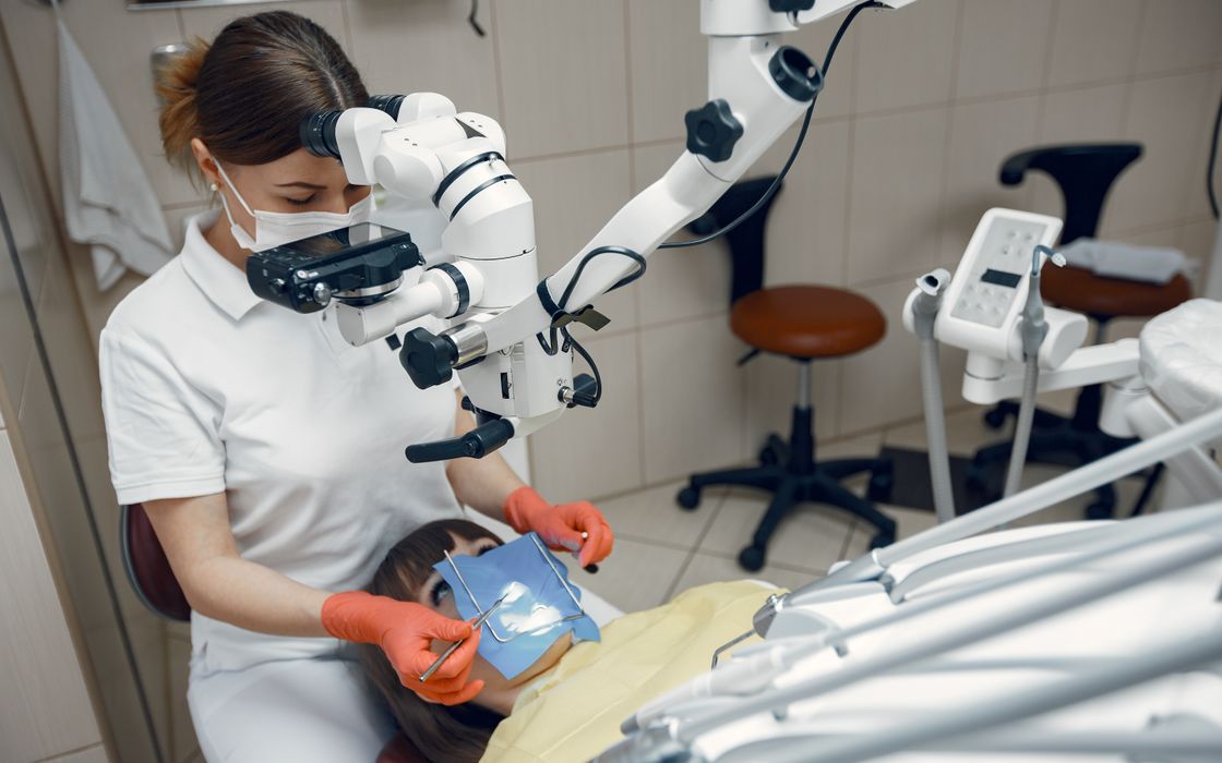 Dentist working with an operating microscope while the patient's tooth is isolated by a blue rubber dam