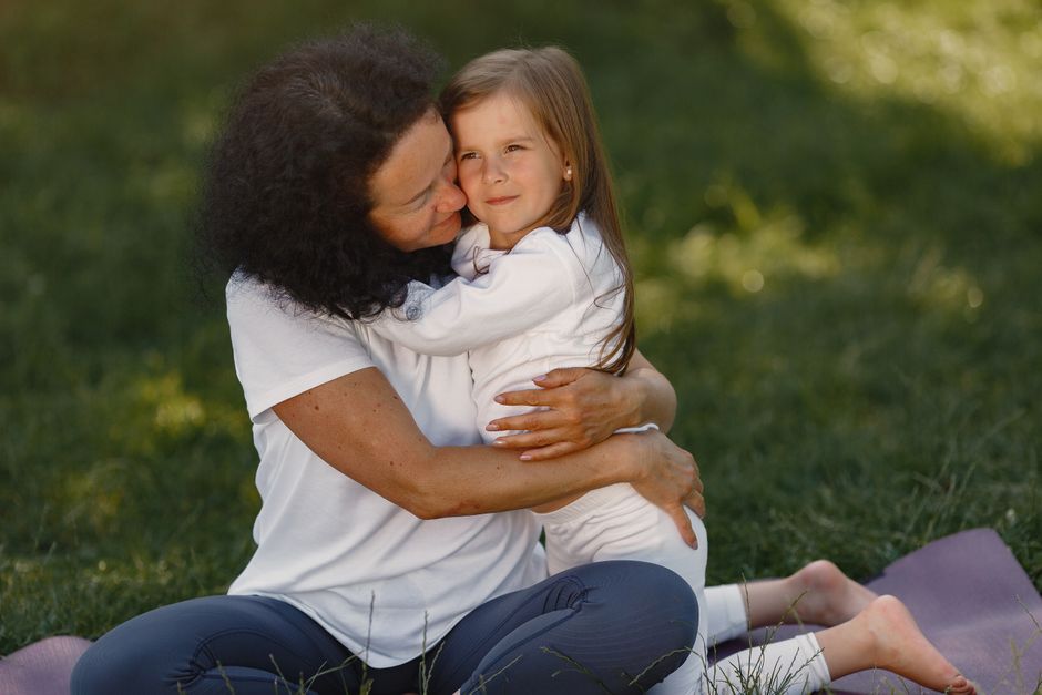 A joyful moment of a mother hugging her young daughter in a sunny outdoor setting.