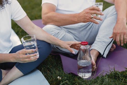 People Holding Glasses of Water while Sitting on Yoga Mats