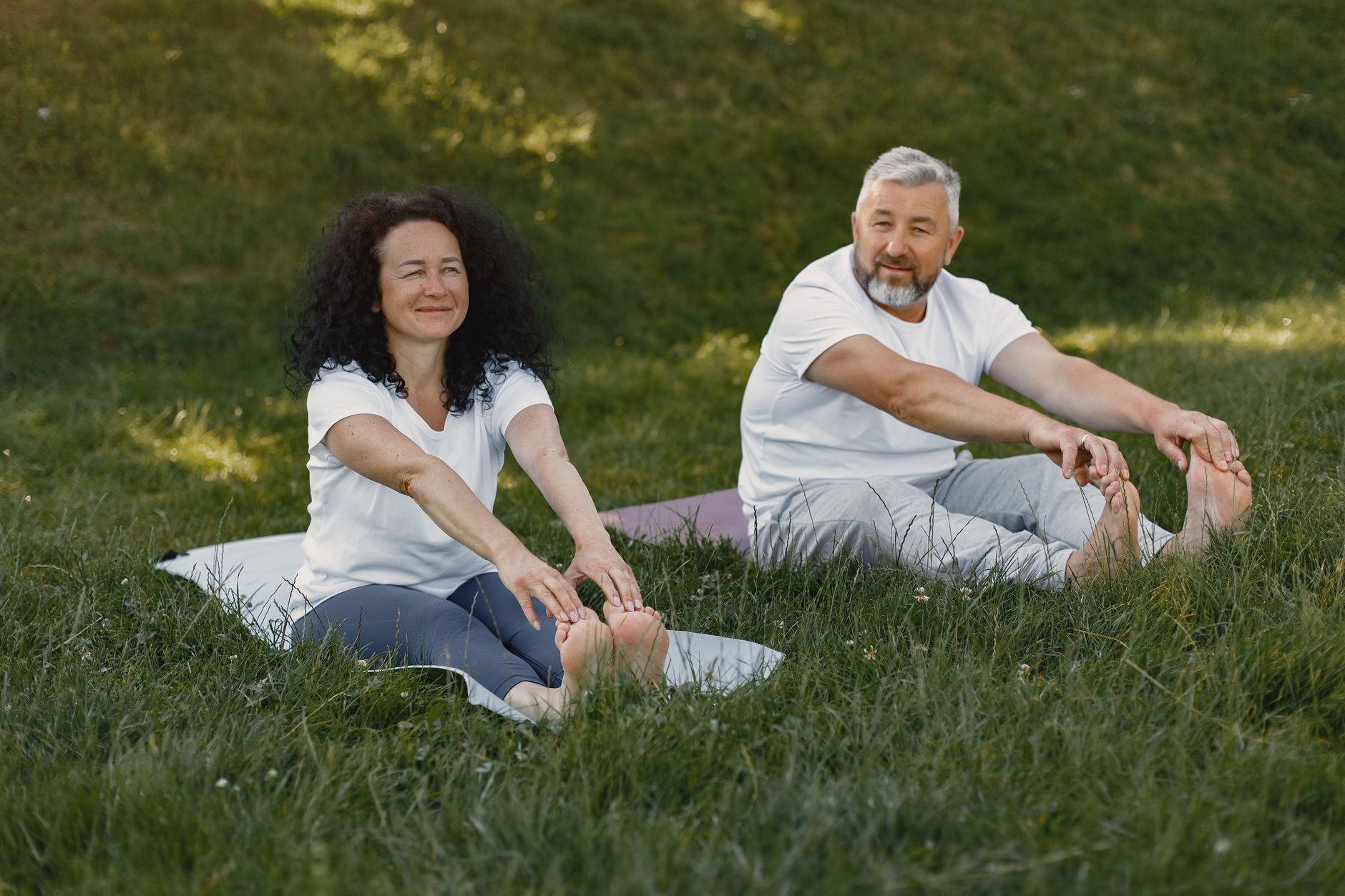 A mature couple enjoying a yoga session together outdoors on a sunny day.