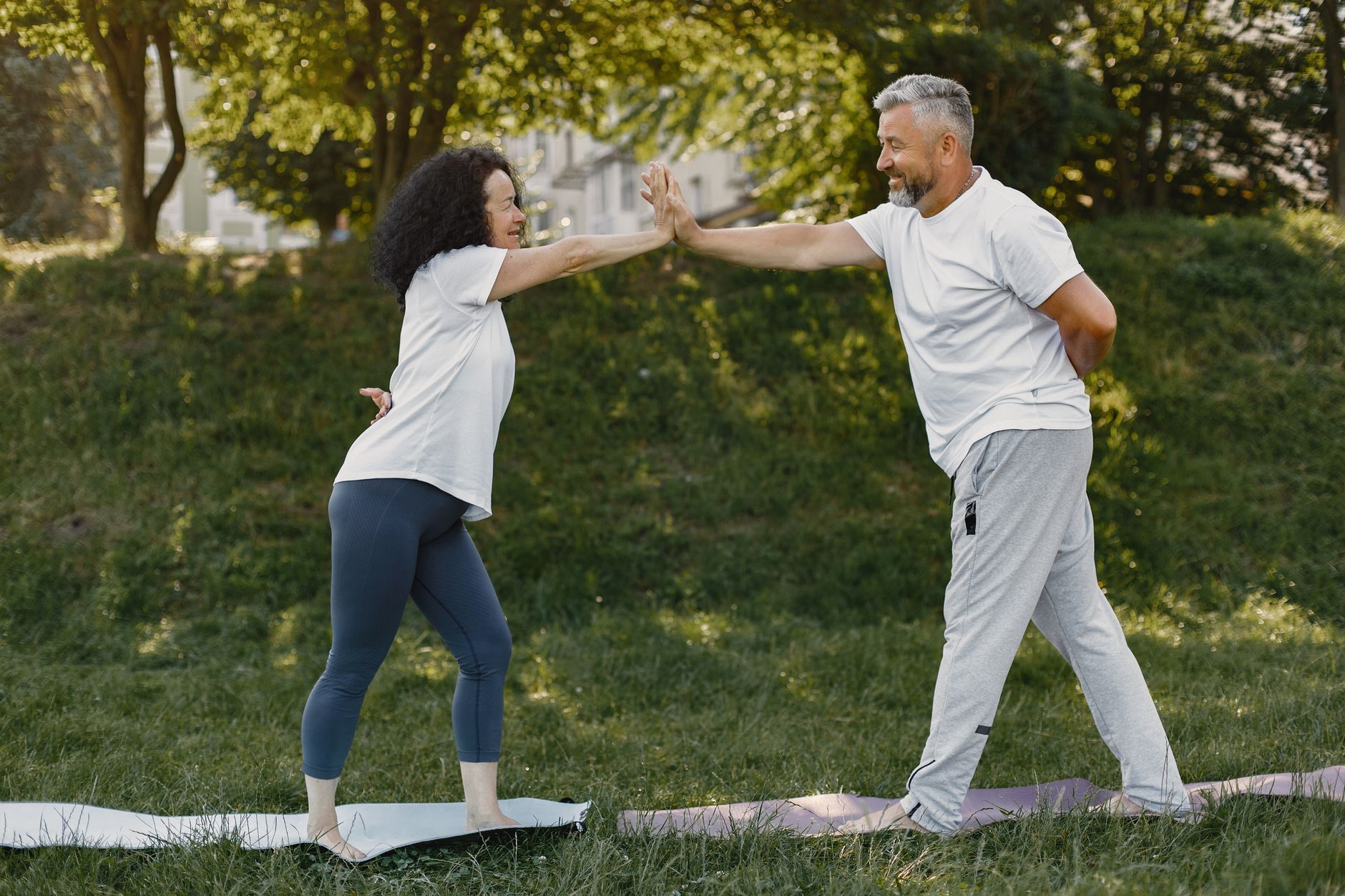 Smiling man and woman giving a high five while exercising outdoors on yoga mats.