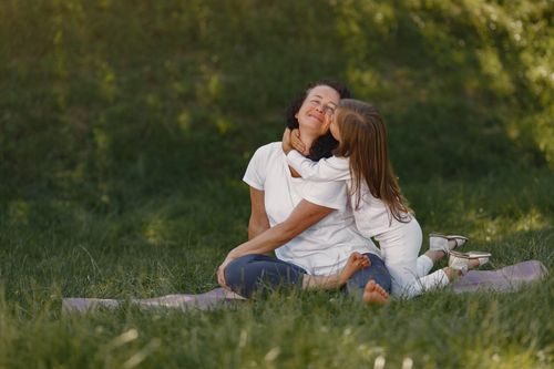 Free A joyful moment between mother and daughter hugging on a grassy field. Stock Photo