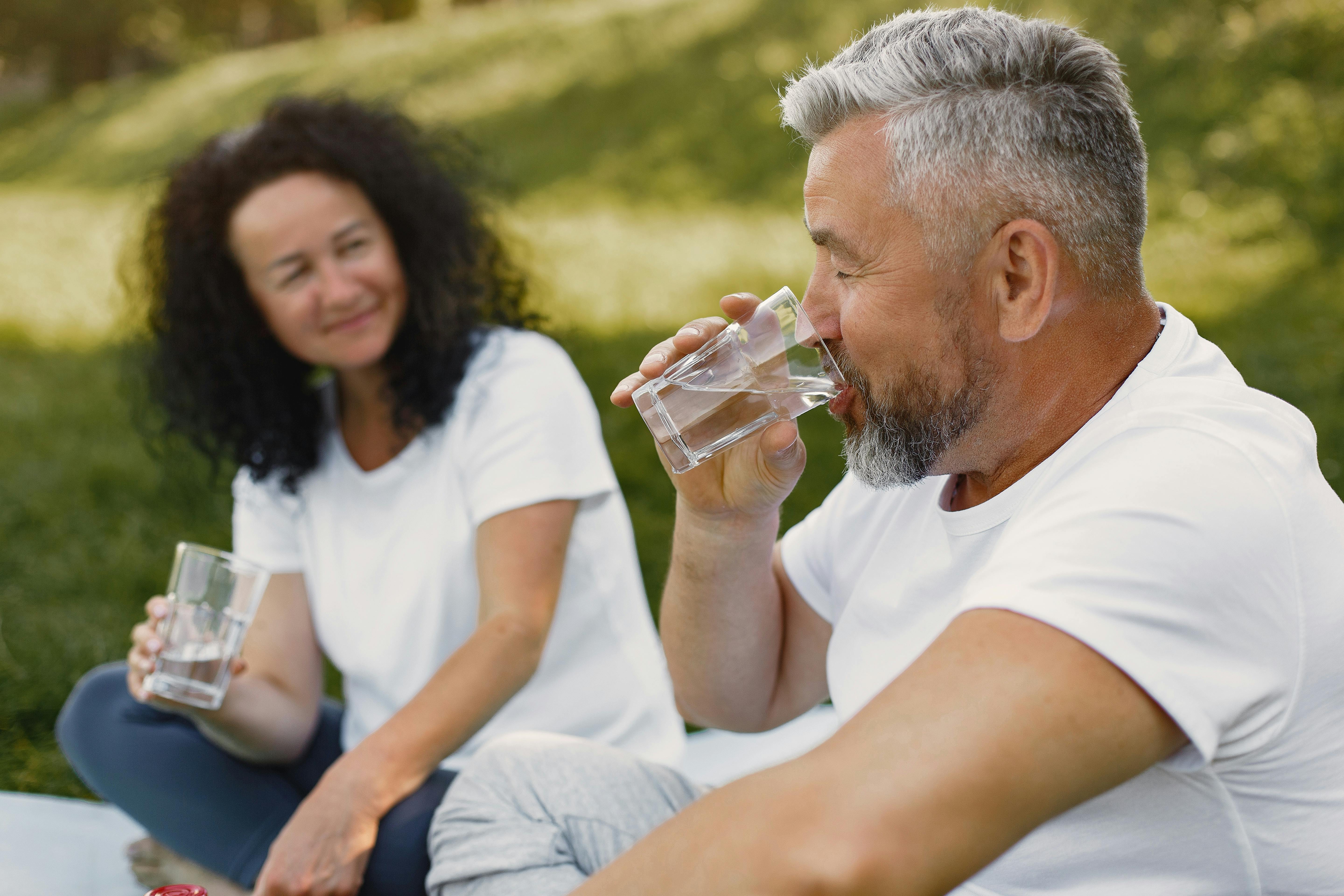 Senior couple sitting outdoors smiling while drinking water together on a sunny day