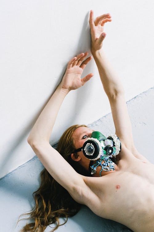 Skinny androgynous man in modish respirator lying on floor gracefully