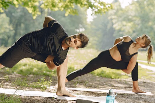Two adults practice yoga poses on mats in a sunlit park.