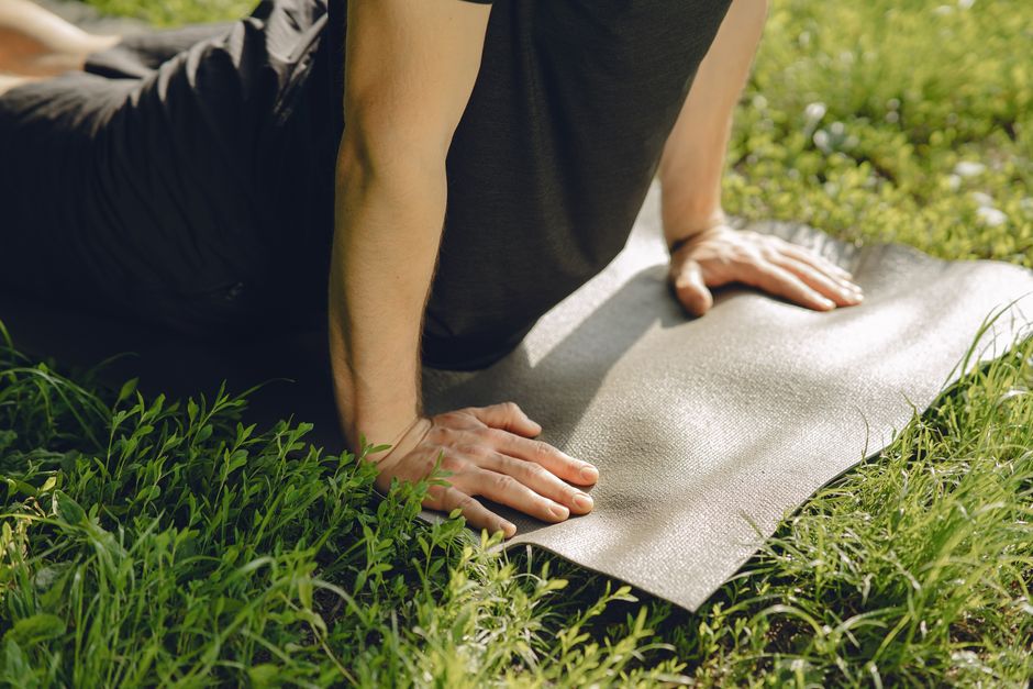 Man practicing yoga outside on a mat in a sunny park.