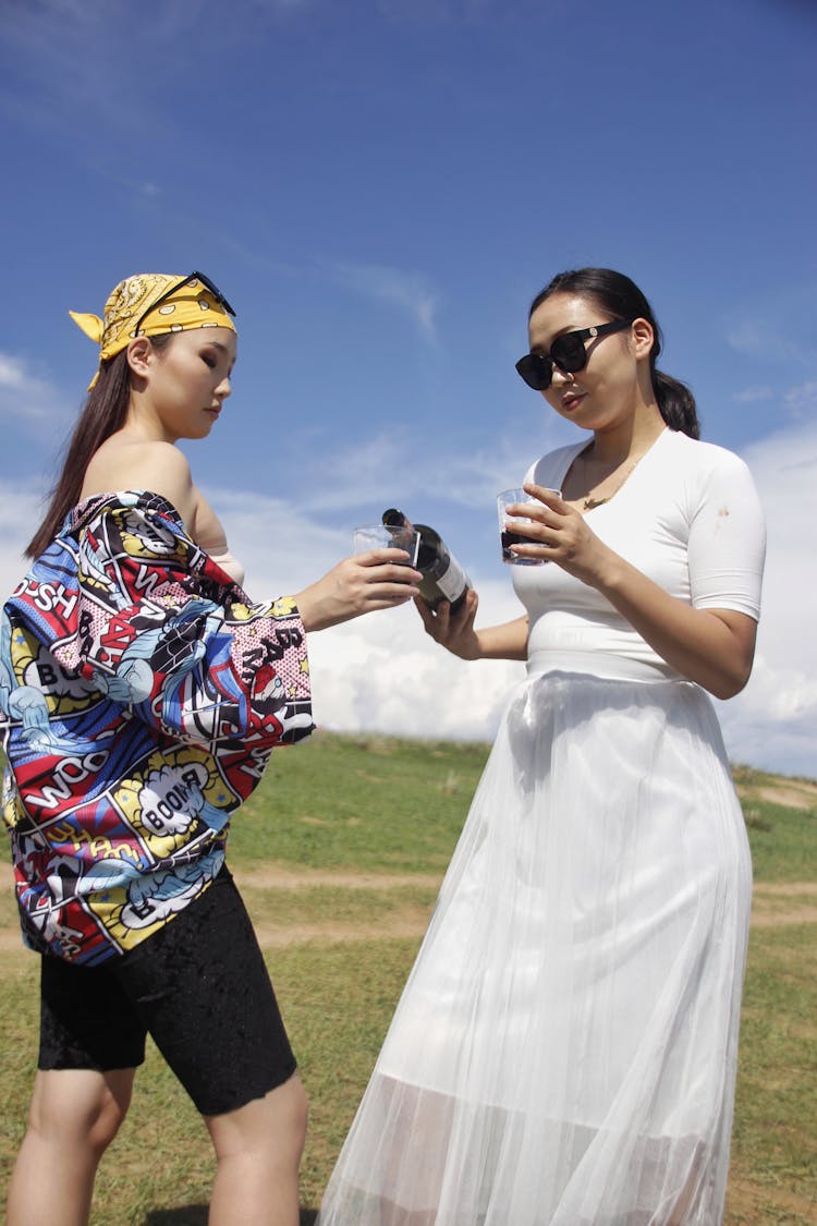 Stylish Asian Women Pouring Red Wine In Glasses In Nature