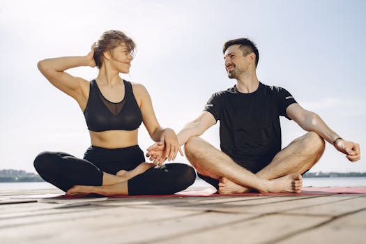 A couple enjoys a peaceful yoga session while holding hands on a sunny pier.
