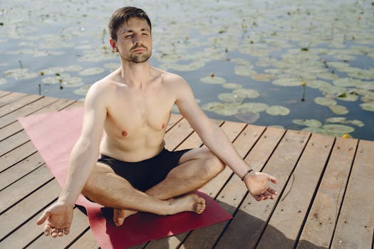 Shirtless man practicing yoga meditation on a pier by a tranquil lake, fostering relaxation and mindfulness.
