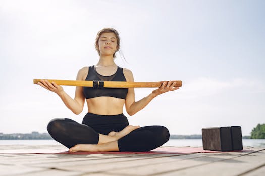 Woman practicing yoga outdoors by a lake with yoga accessories, enjoying a serene environment.