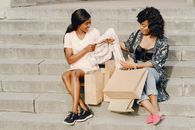Brunettes Sitting on Concrete Steps and Looking on Shopping Items