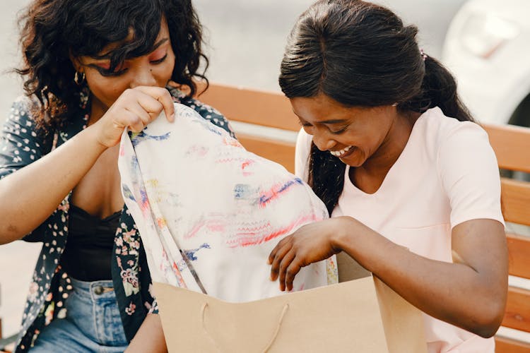 Two Women Taking Out Clothes From A Shopping Bag