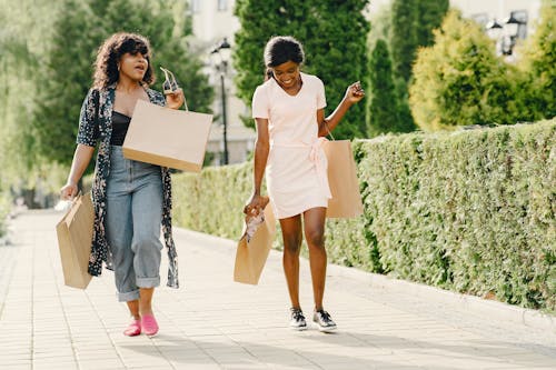 Free Two Women Walking Together with Shopping Paper Bags and Smile Stock Photo