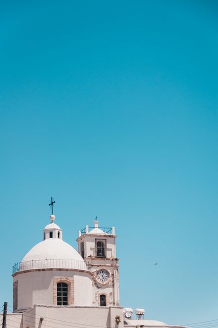 A white church with a dome and bell tower against a bright blue sky, providing ample copy space.