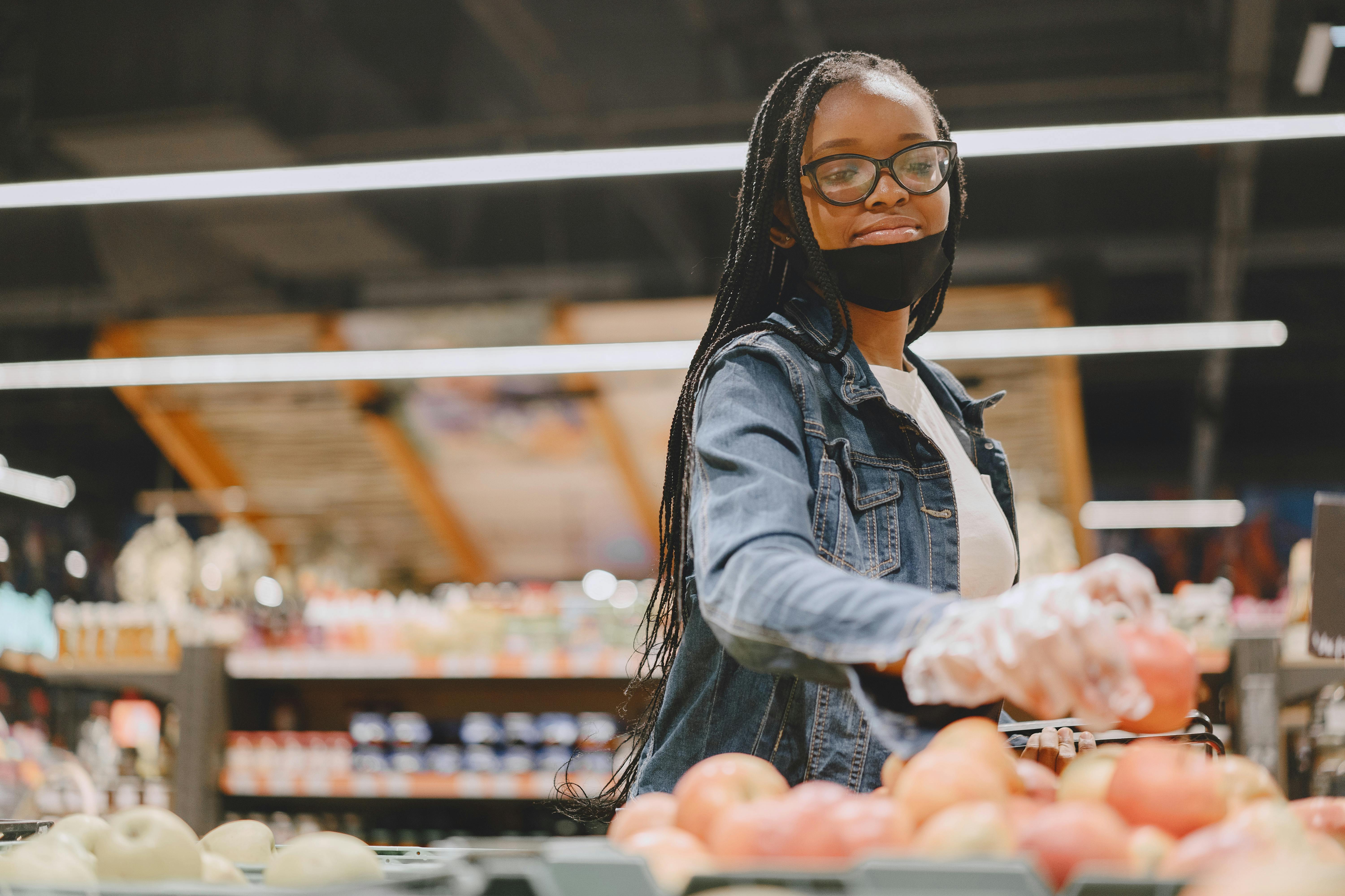 Woman wearing mask and gloves shops for fresh fruit in a grocery store.