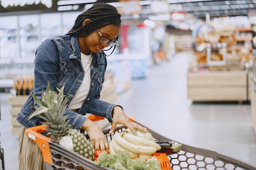 A woman shops for fresh fruits and vegetables in a supermarket, pushing a cart filled with groceries.