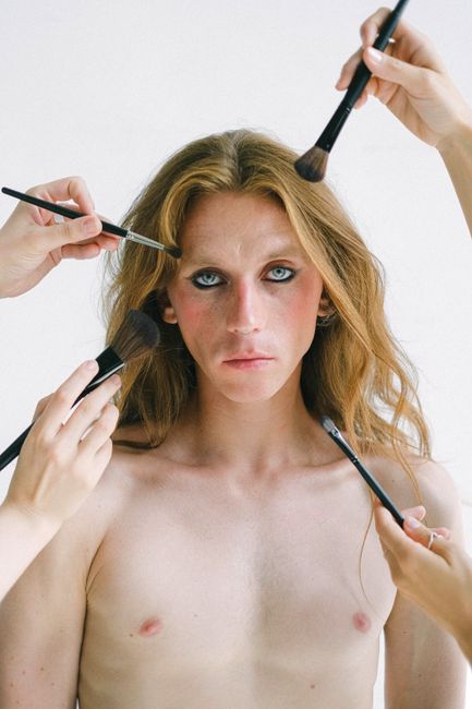 Close-up portrait of a model with long hair surrounded by makeup brushes in a studio setting.