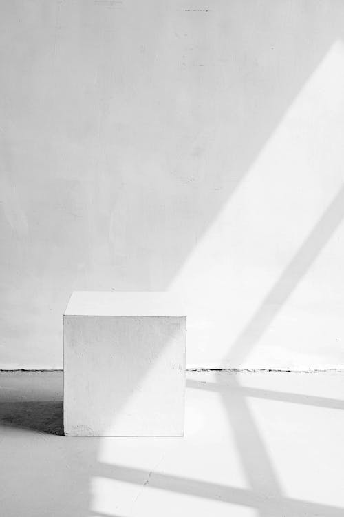 Simple white cube stool placed against wall in light studio on sunny day