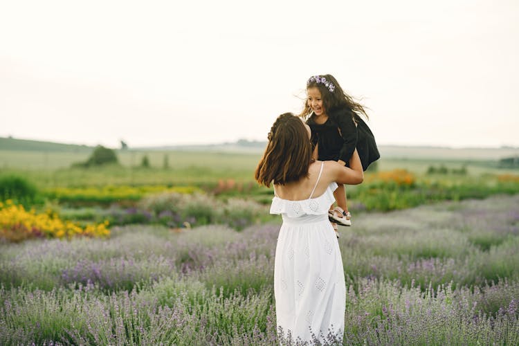 A Woman In White Dress Lifting A Girl In A Black Dress