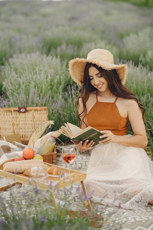 Woman in Sun Hat and Skirt Reading a Book on a Picnic Blanket