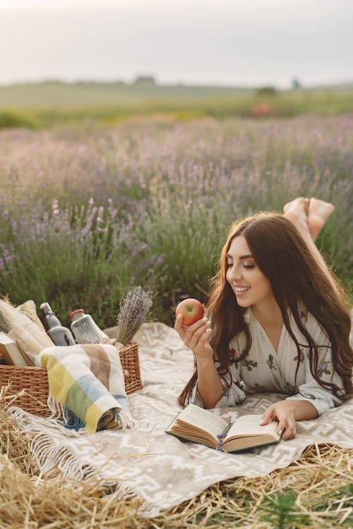 Woman Holding an Apple Lying on a Picnic Blanket