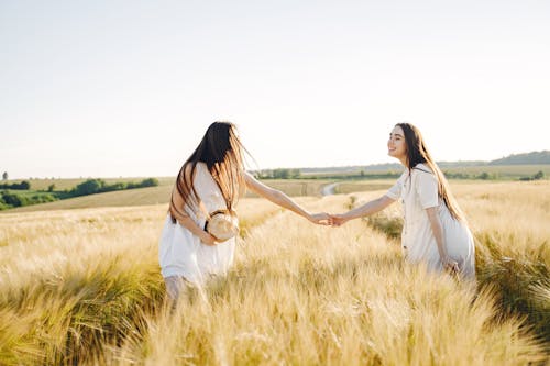 Women in White Dress Holding Hands on a Grass Field