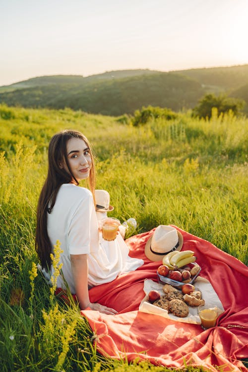 A Woman in White Dress Sitting on a Red Picnic Blanket