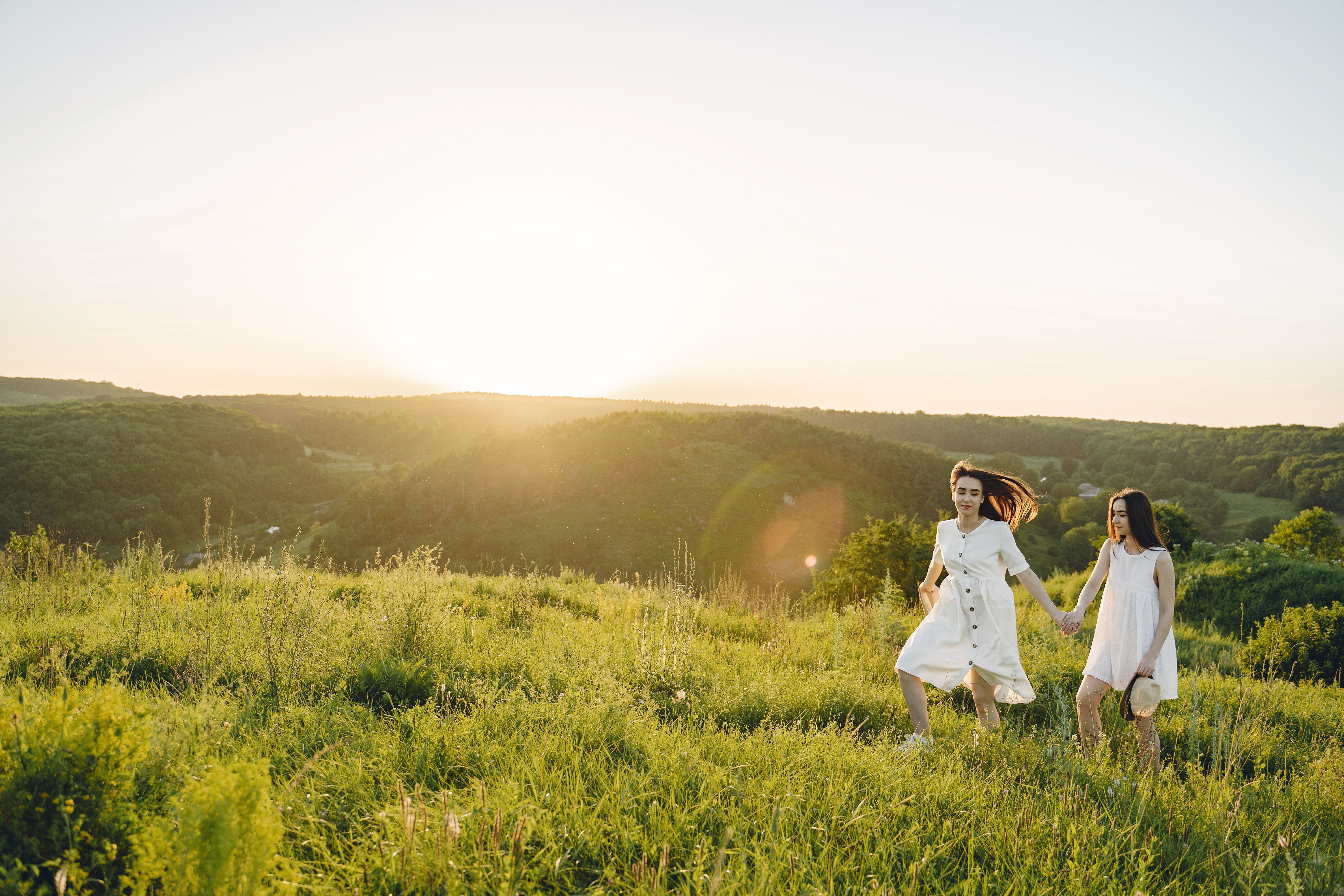 Two Women Holding Hands While Walking on a Green Field · Free Stock Photo