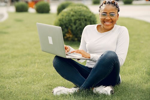 Free A Woman in White Long Sleeves Holding a Laptop Sitting on a Grass Stock Photo