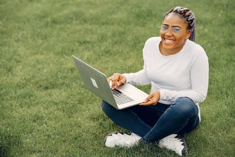 Smiling Girl Sitting On Grass Working On Laptop