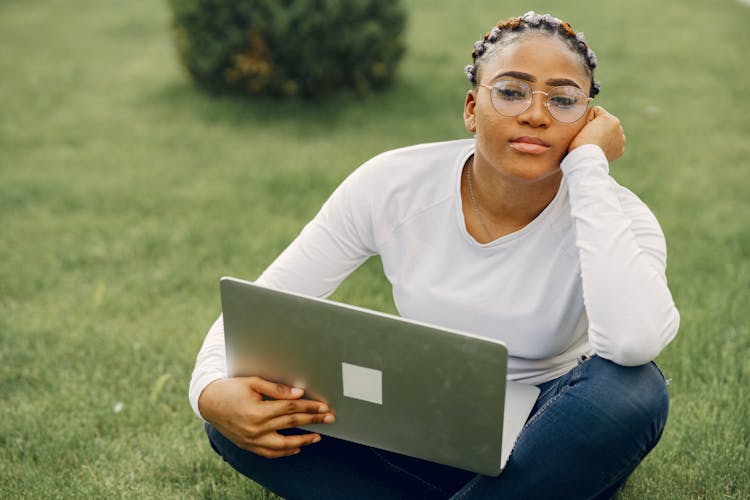 Portrait Of Woman With Colorful Braids Sitting On Grass With Laptop