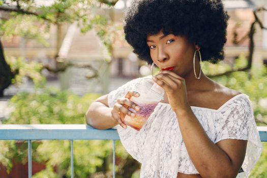 Stylish woman savoring a colorful drink outdoors on a sunny day, exuding happiness and leisure.