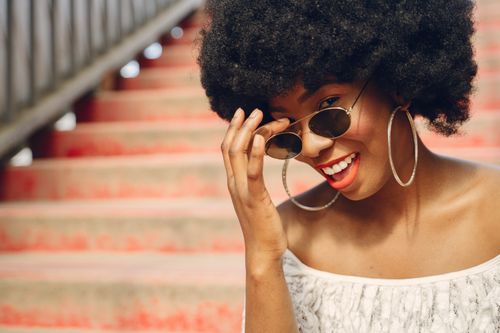Free Charming woman with afro hairstyle and sunglasses smiling on colorful stairs. Stock Photo