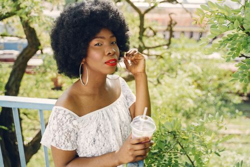 Free Black woman with afro hair holding a drink in an outdoor setting. Stock Photo
