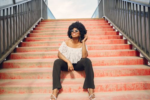 Free Cheerful woman with afro hairstyle sitting on vibrant stairs outdoors, wearing sunglasses. Stock Photo