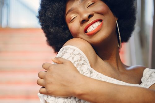 Free Close-up of a smiling woman with afro hair in a white lace top, radiating joy. Stock Photo