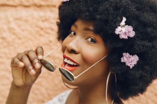 Free A smiling woman with an afro hairstyle decorated with flowers, exuding happiness and summer vibes. Stock Photo