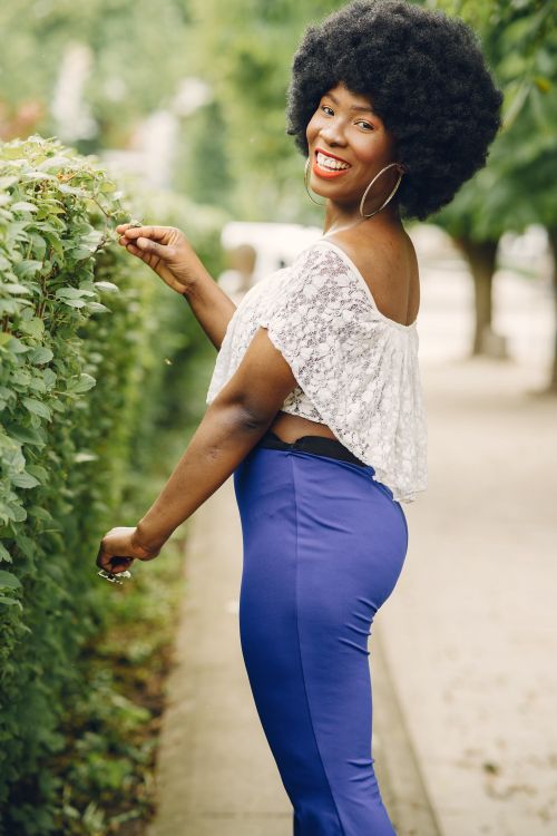 Free Smiling woman with curly hair poses outdoors in chic outfit on a city street. Stock Photo