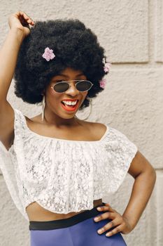 Cheerful woman with afro hairstyle adorned with flowers, smiling in a summer outfit.
