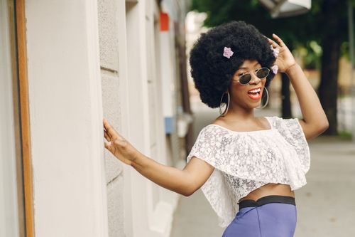 Free Fashionable woman with afro hairstyle, wearing sunglasses, poses in a white lace top and blue skirt. Stock Photo