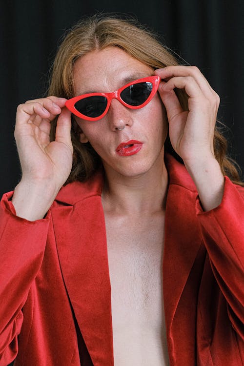 Fashionable young androgynous guy adjusting sunglasses in studio